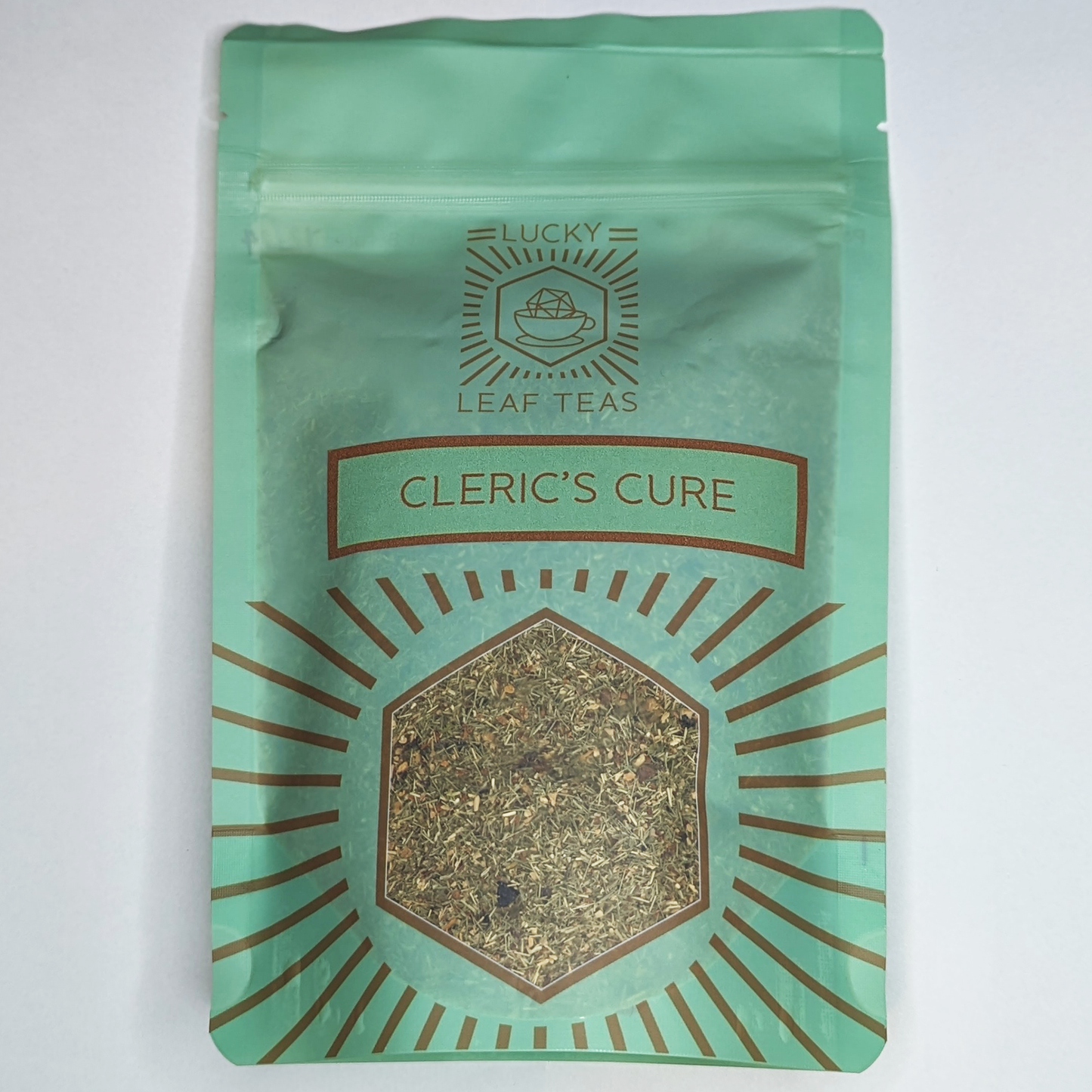 A mint-green package containing 100g of Cleric’s Cure: a herbal infusion blend. The name is stickered on the front, below the Lucky Leaf Teas Logo and above a hexagonal window displaying the tea.