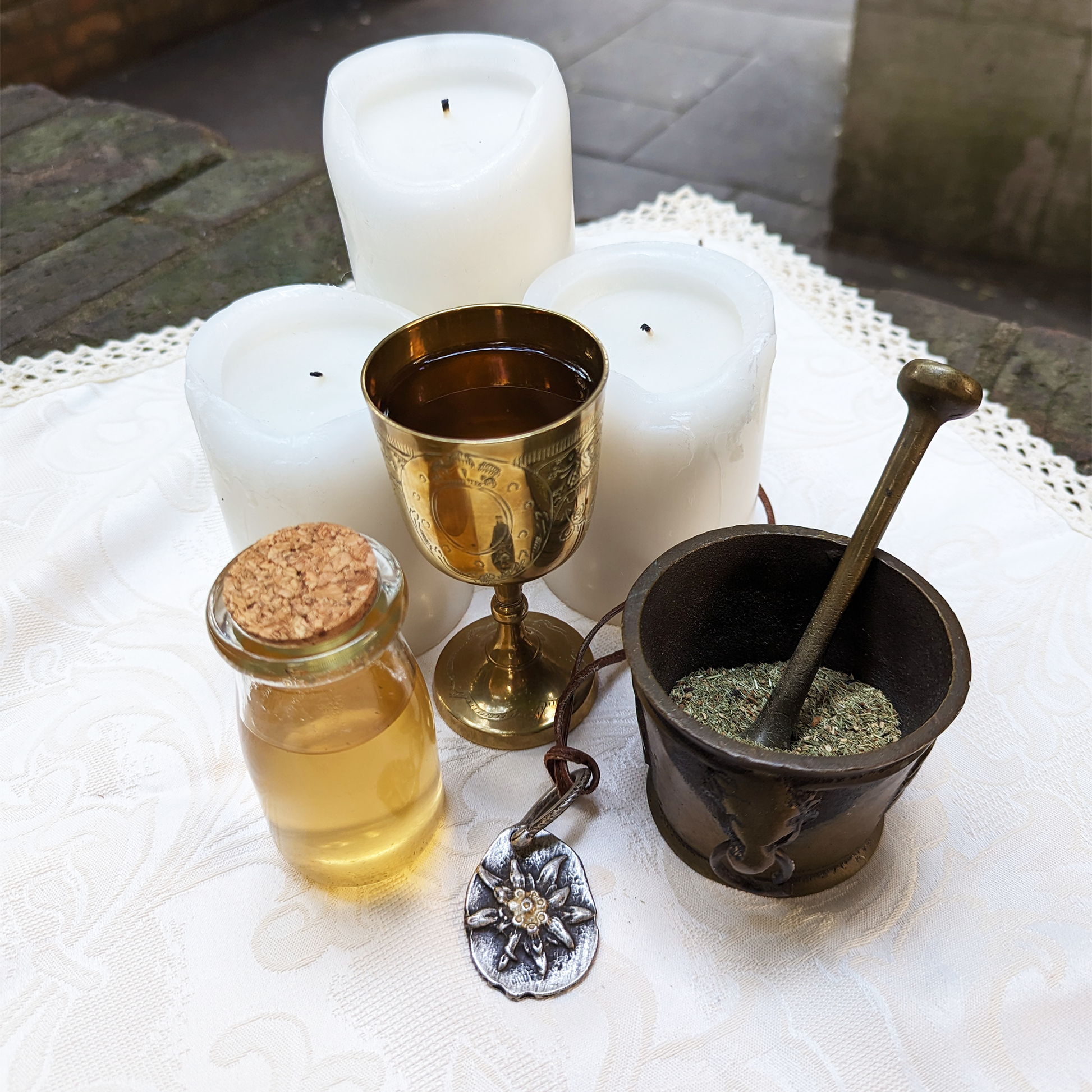 A brass chalice filled with honey-coloured infusion, next to a glass potion bottle, and a pestle and mortar with a herbal blend inside.