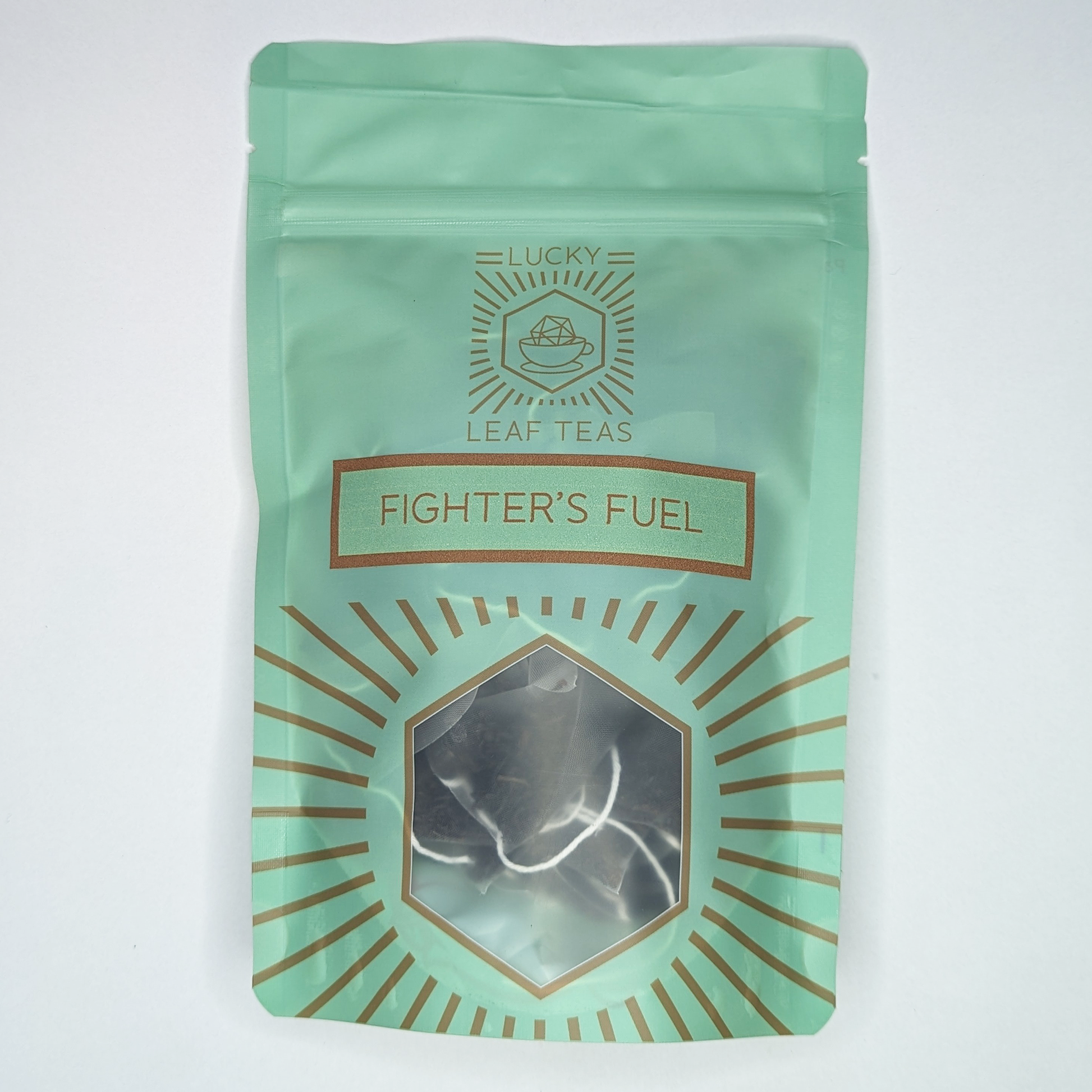 A mint-green package containing 15 Silky Pyramid Teabags of Fighter’s Fuel: a black tea blend. The name is stickered on the front, below the Lucky Leaf Teas Logo and above a hexagonal window displaying the tea.