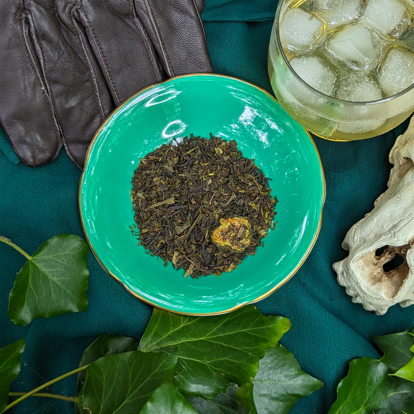 A close-up view of a mound of green tea leaves on a green saucer. There are pieces of dried cucumber mixed in.