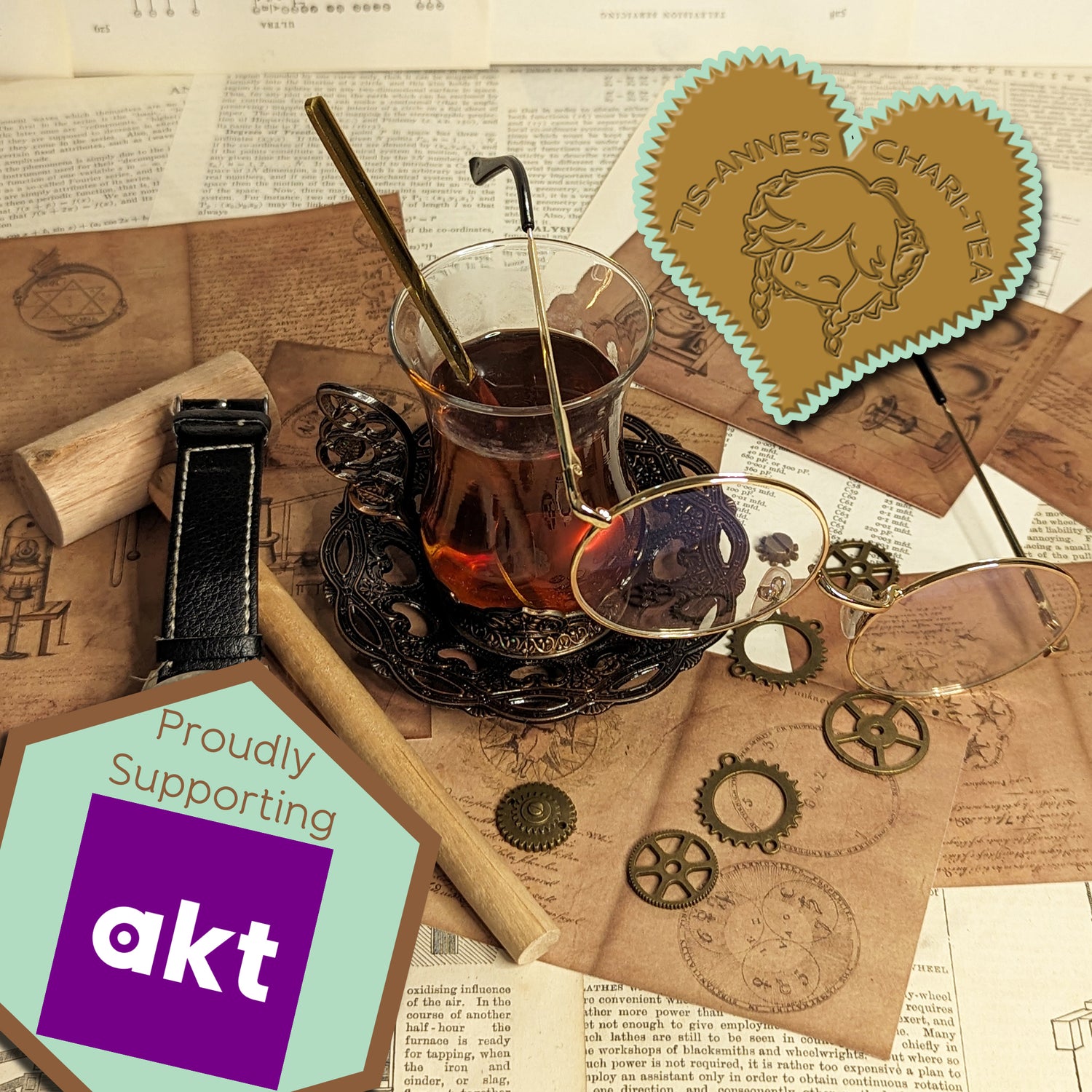 A tall, glass cup of tea and a wrought-iron dish are on top of sheets of paper covered in alchemical and engineering designs. A heart-shaped badge in one corner reads "Tis-Anne's Chari-Tea", and another emblem reads "Proudly Supporting" with the logo for akt.
