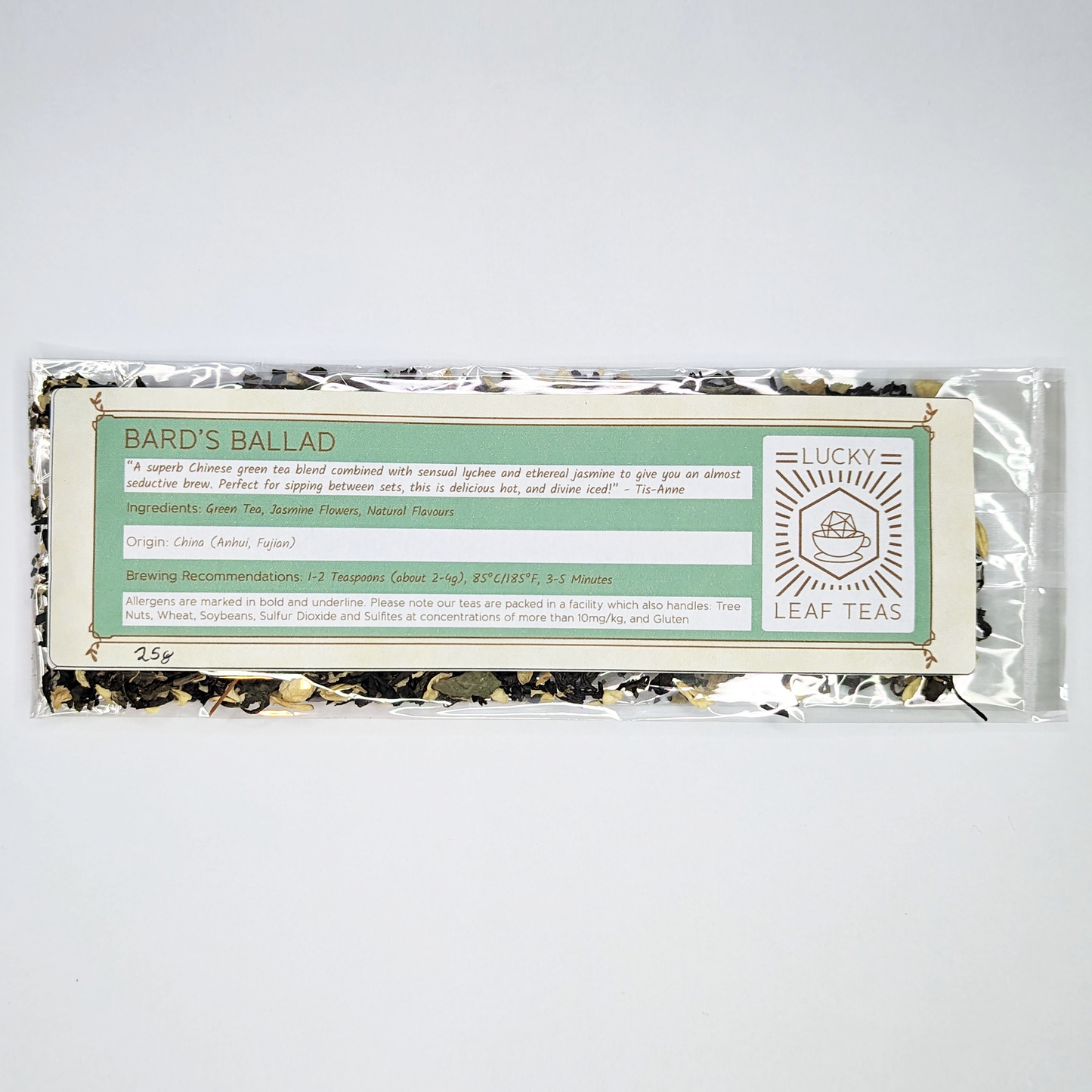 A slim, see-through package containing 25g of Bard’s Ballad: a green tea blend with visible jasmine flowers. A label with the name, ingredients, origin and brewing recommendations is printed on the front, next to the Lucky Leaf Teas Logo.