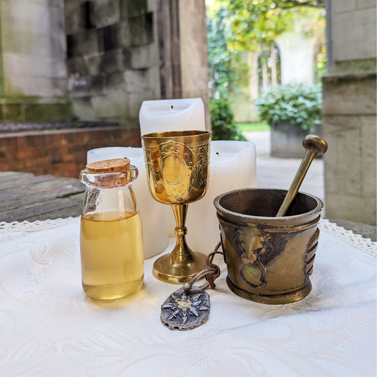 A brass chalice, next to a glass potion bottle filled with a yellow infusion, and a mortar and pestle. Tall cathedral windows are in the background.