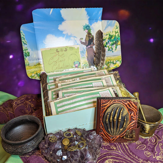 An open mint-coloured box, with an illustration of a horned character with a teacup smiling towards the viewer. The box is filled with slim packaged of tea and herbal blends, and is surrounded by a chunk of amethyst, gears, a leather-bound book with a skeletal hand on it, a brass mortar and pestle, and a small black cauldron. A card on the box reads: "The Caster's Collection."