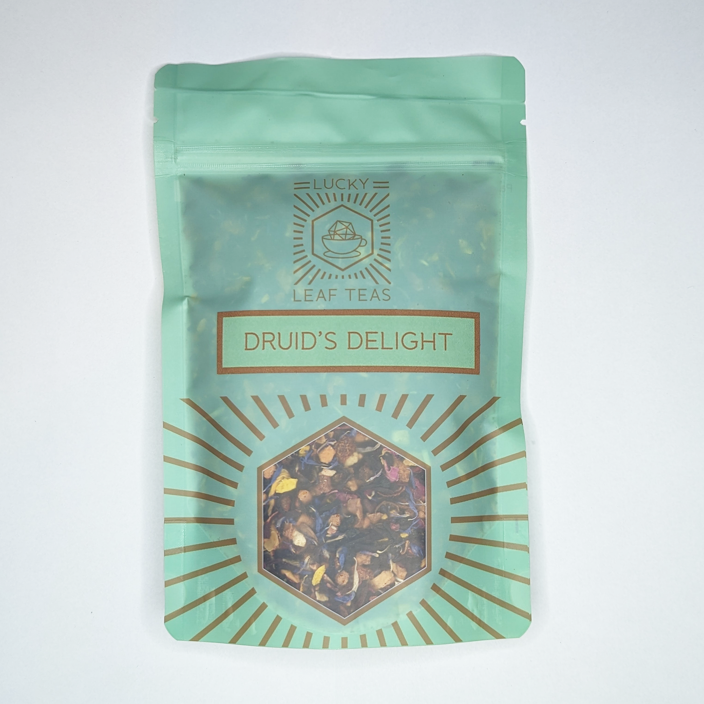 A mint-green package containing 100g of Druid’s Delight: an infusion blend of dried fruits and flower petals. The name is stickered on the front, below the Lucky Leaf Teas Logo and above a hexagonal window displaying the tea.