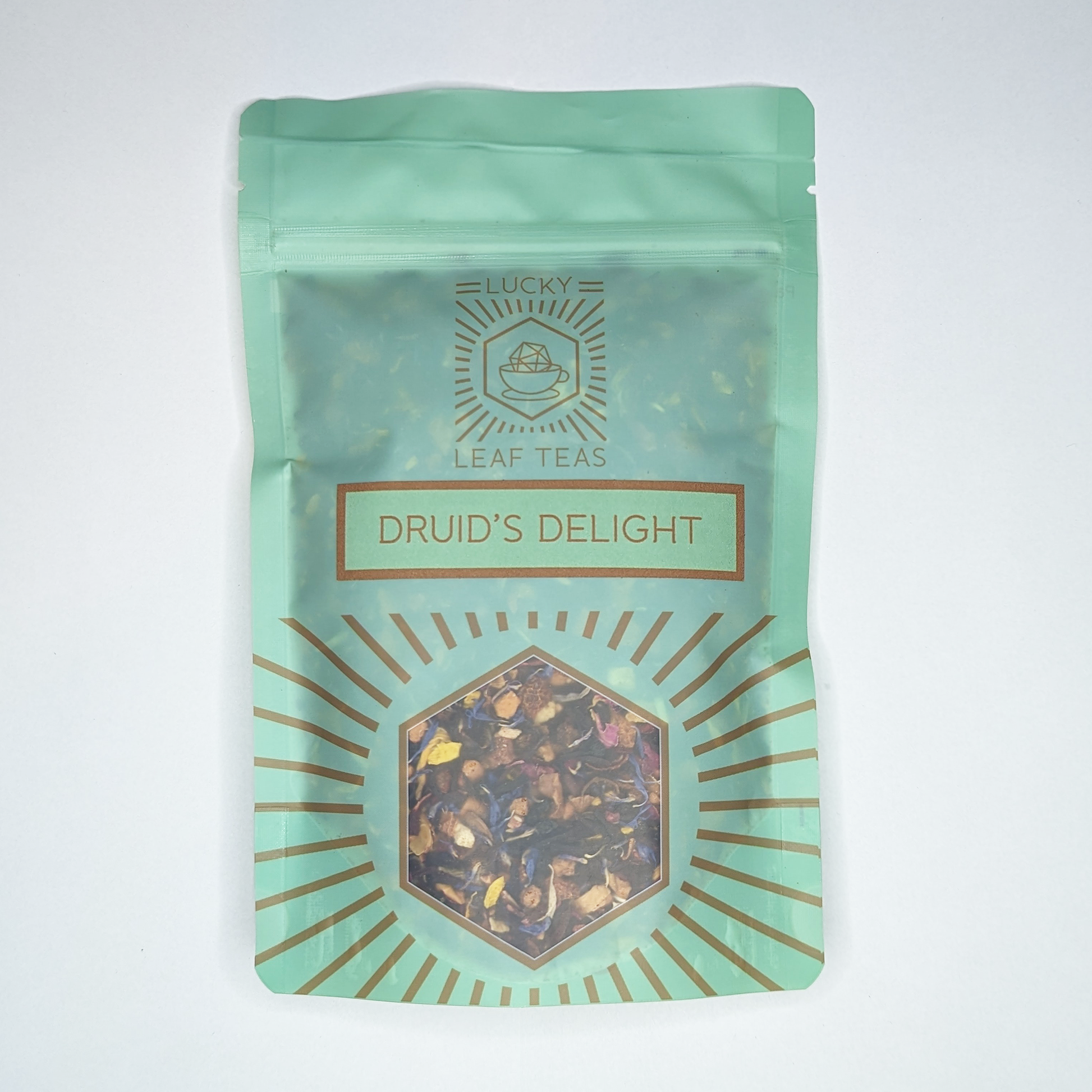 A mint-green package containing 100g of Druid’s Delight: an infusion blend of dried fruits and flower petals. The name is stickered on the front, below the Lucky Leaf Teas Logo and above a hexagonal window displaying the tea.