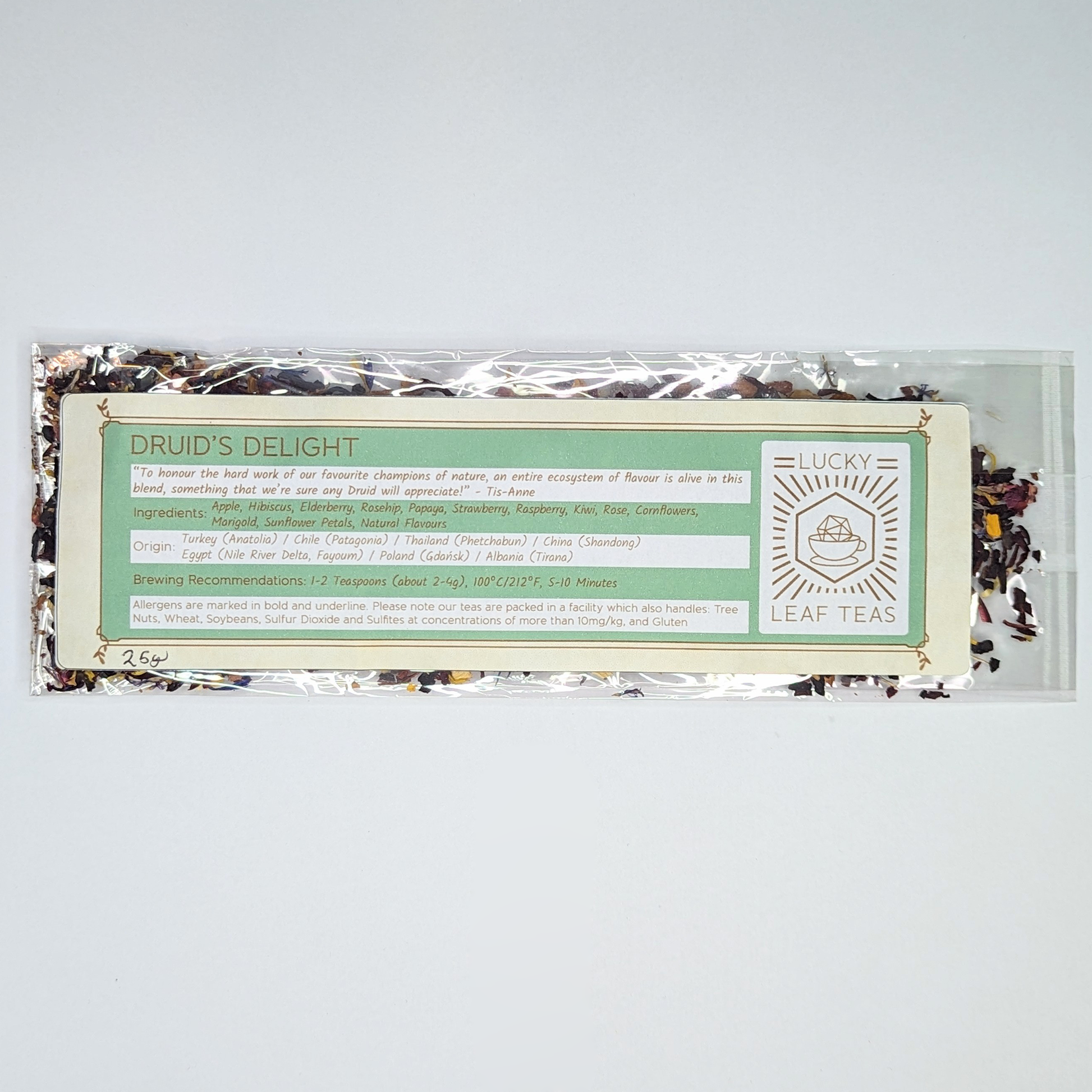 A slim, see-through package containing 25g of Druid’s Delight: an infusion blend of dried fruits and flower petals. A label with the name, ingredients, origin and brewing recommendations is printed on the front, next to the Lucky Leaf Teas Logo.