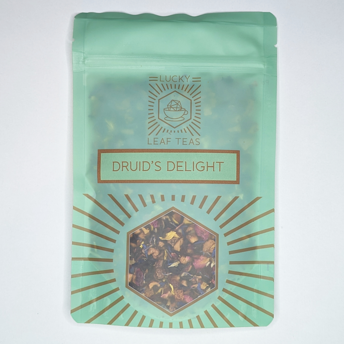 A mint-green package containing 50g of Druid’s Delight: an infusion blend of dried fruits and flower petals. The name is stickered on the front, below the Lucky Leaf Teas Logo and above a hexagonal window displaying the tea.