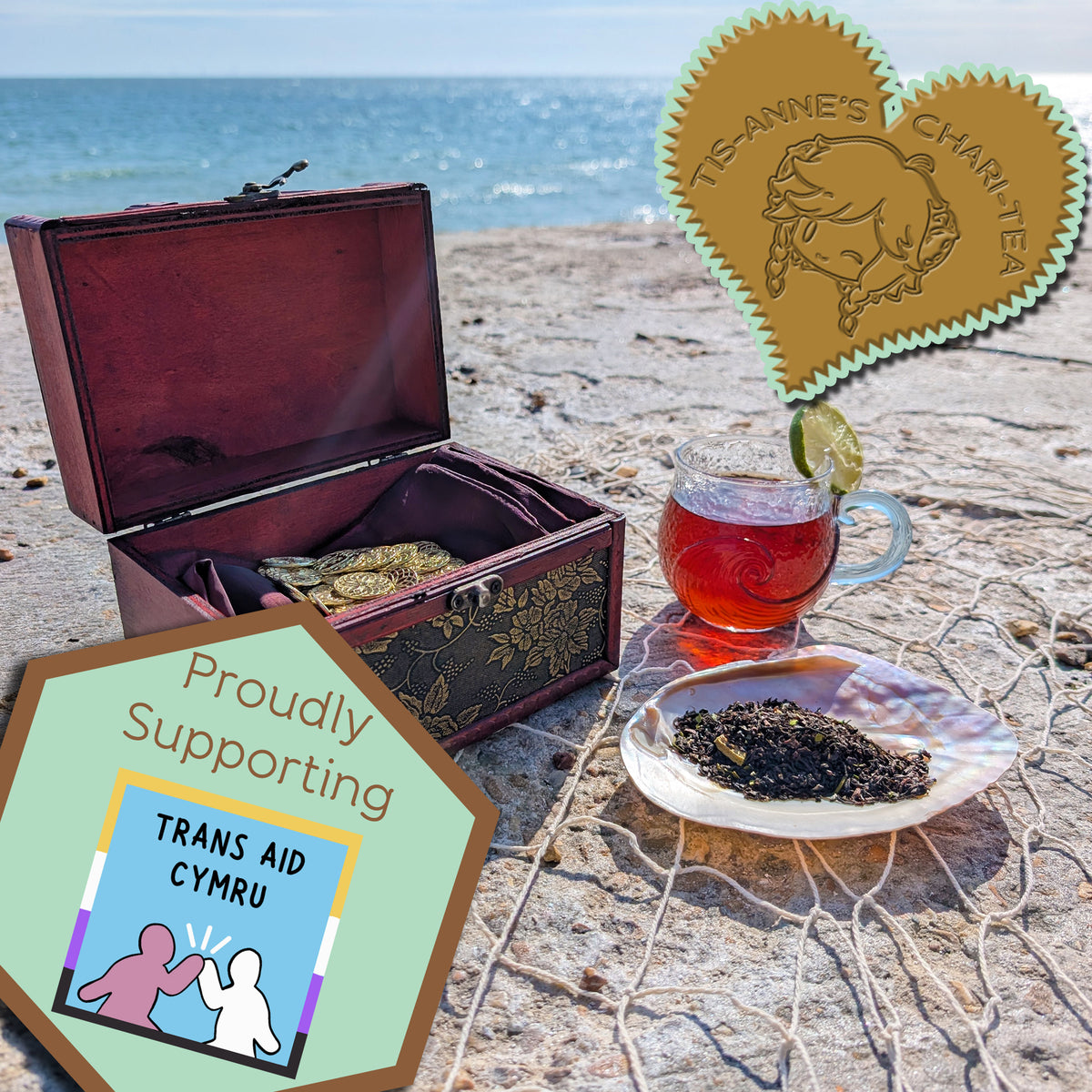 An open red-wood box with a decorative front reveals gold coins on a red satin pillow. Adjacent is a mother-of-pearl shell filled with tea leaves and behind sits a glass cup with a wave motif, filled with amber-red tea and a lime wedge on the rim. In the background you can see the sea and sky, and a bird flying past. Everything sits on a rope net.
A heart-shaped badge in one corner reads "Tis-Anne's Chari-Tea", and an emblem in the other reads "Proudly Supporting - Trans Aid Cymru."