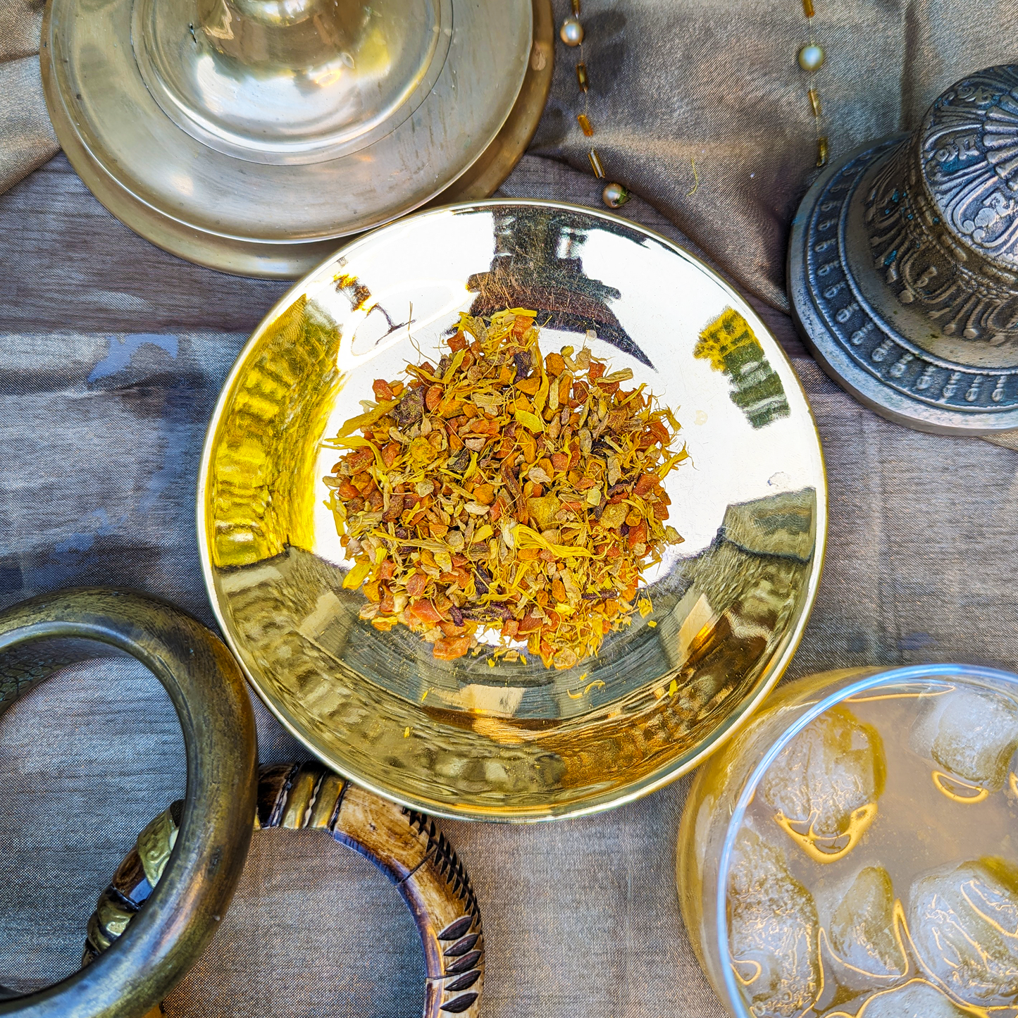 A golden saucer with a herbal infusion blend mounded on it. Pieces of carrot, pineapple, ginger, beetroot and yellow flower petals can be seen.