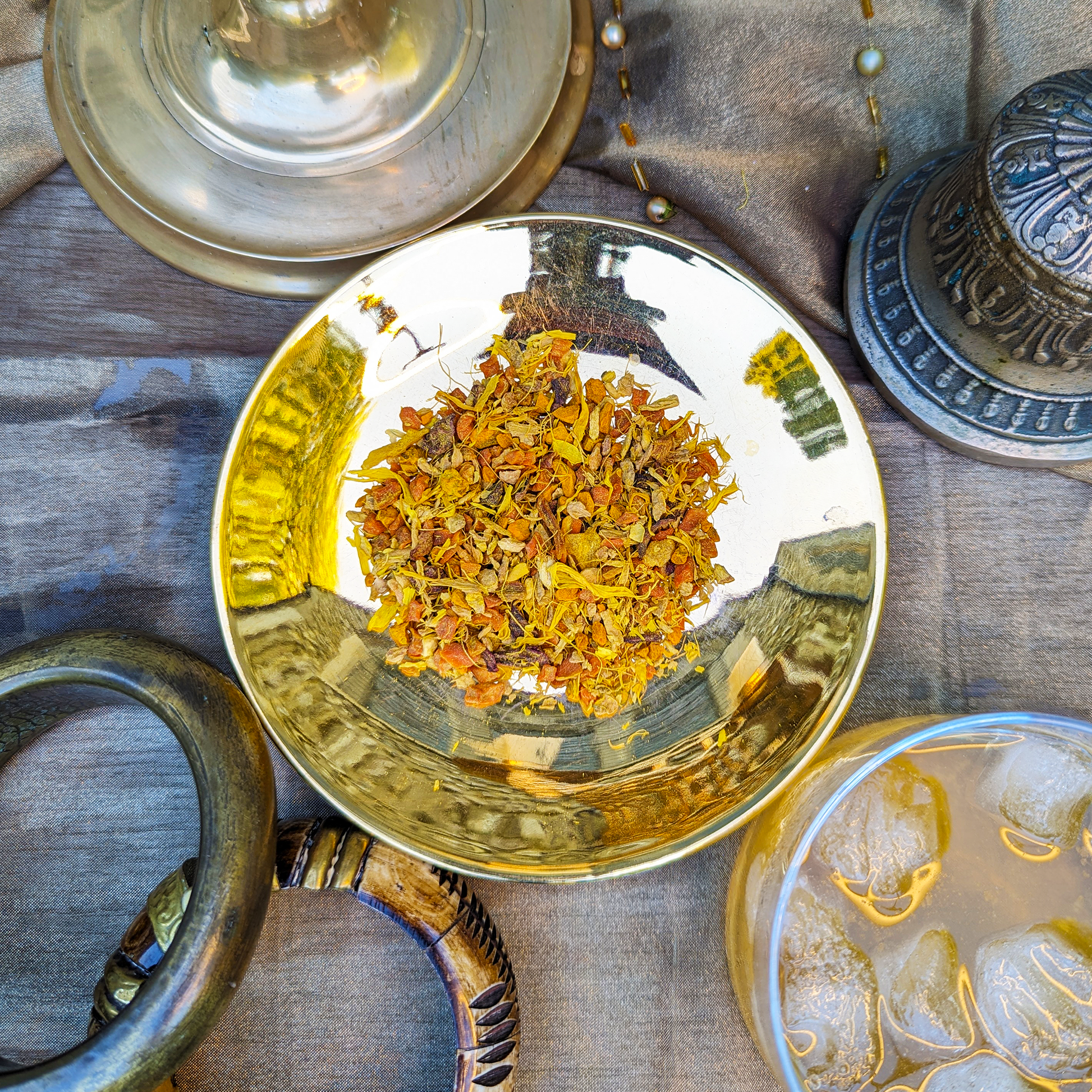 A golden saucer with a herbal infusion blend mounded on it. Pieces of carrot, pineapple, ginger, beetroot and yellow flower petals can be seen.