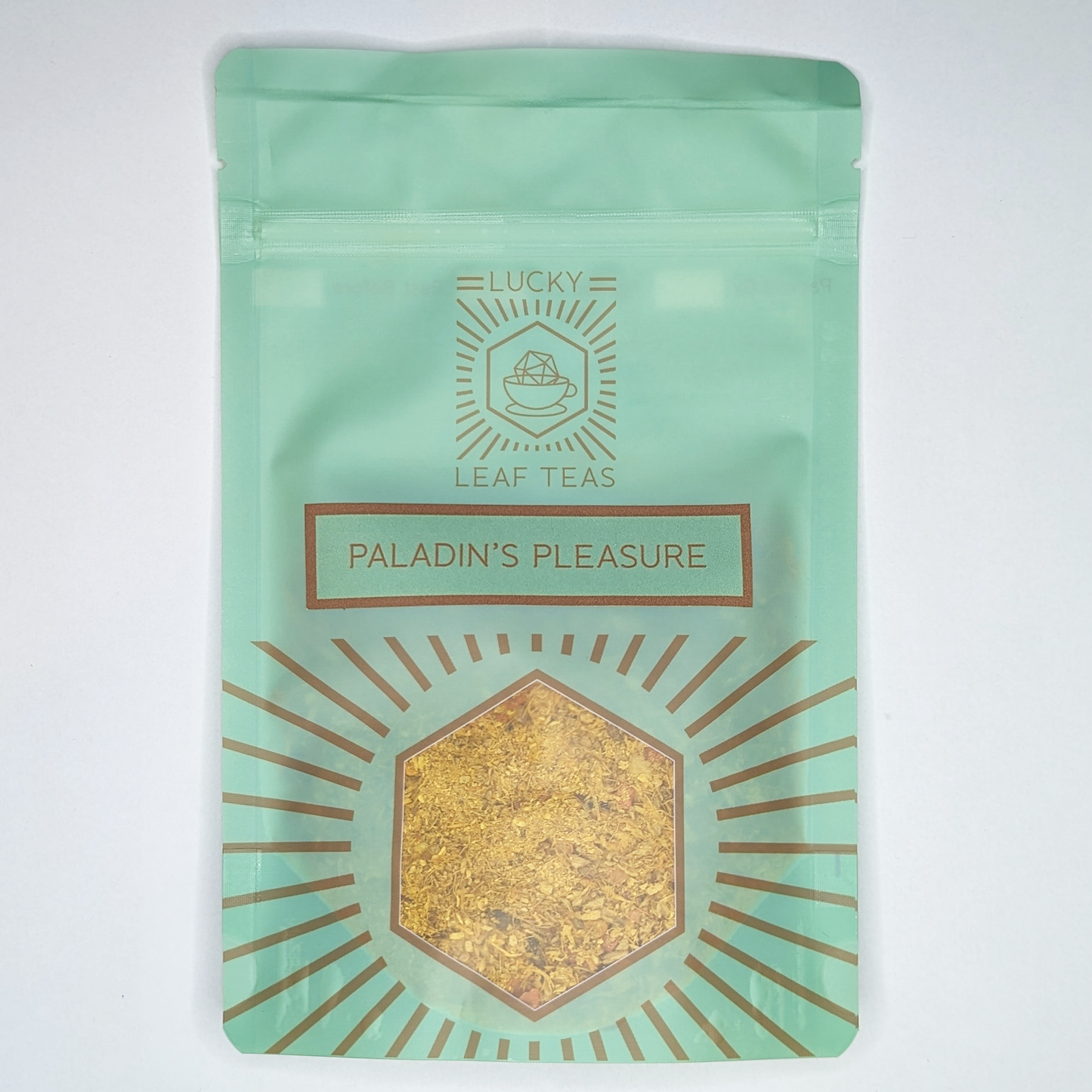 A mint-green package containing 50g of Paladin’s Pleasure: a bright yellow infusion blend of spices, fruits and flowers. The name is stickered on the front, below the Lucky Leaf Teas Logo and above a hexagonal window displaying the tea.