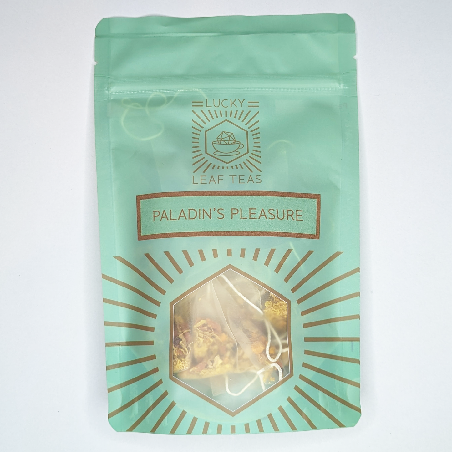 A mint-green package containing 15 Silky Pyramid Teabags of Paladin’s Pleasure: a bright yellow infusion blend of spices, fruits and flowers. The name is stickered on the front, below the Lucky Leaf Teas Logo and above a hexagonal window displaying the tea.