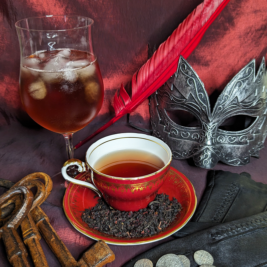 A red teacup and saucer next to a wine glass, both filled with copper red tea, one hot, one iced.