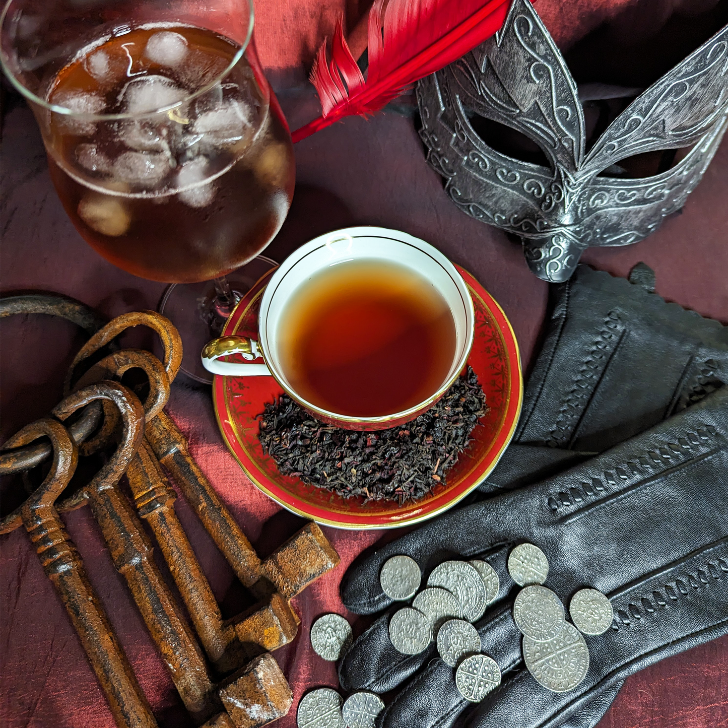 A red teacup and saucer, filled with tea, surrounded by a pair of gloves, old keys and loose coins.