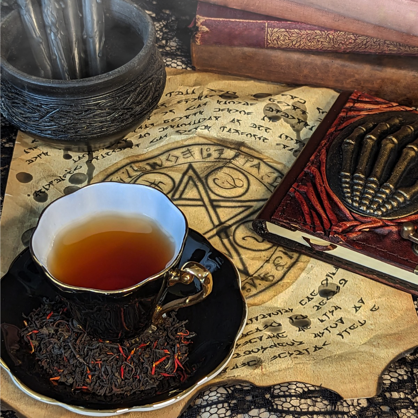 A black teacup of tea and a matching saucer on top of wax-covered aged paper with summoning circles on it. Tea leaves mixed with red flowers are on the saucer.