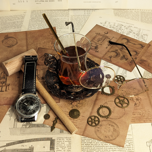 A tall, glass cup of tea and a wrought-iron dish are on top of sheets of paper covered in alchemical and engineering designs.