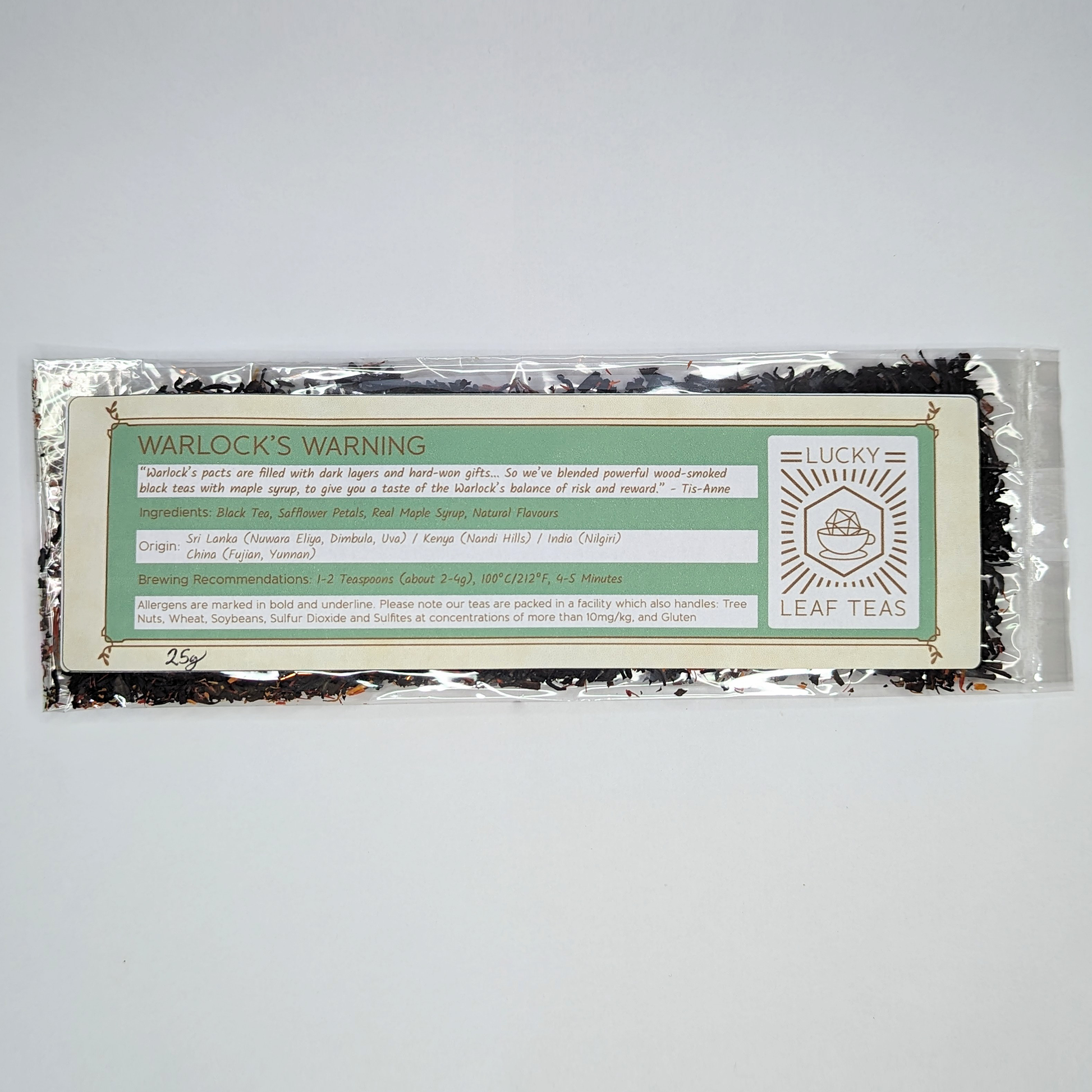 A slim, see-through package containing 25g of Warlock’s Warning: a black tea blend with visible red safflower petals. A label with the name, ingredients, origin and brewing recommendations is printed on the front, next to the Lucky Leaf Teas Logo.