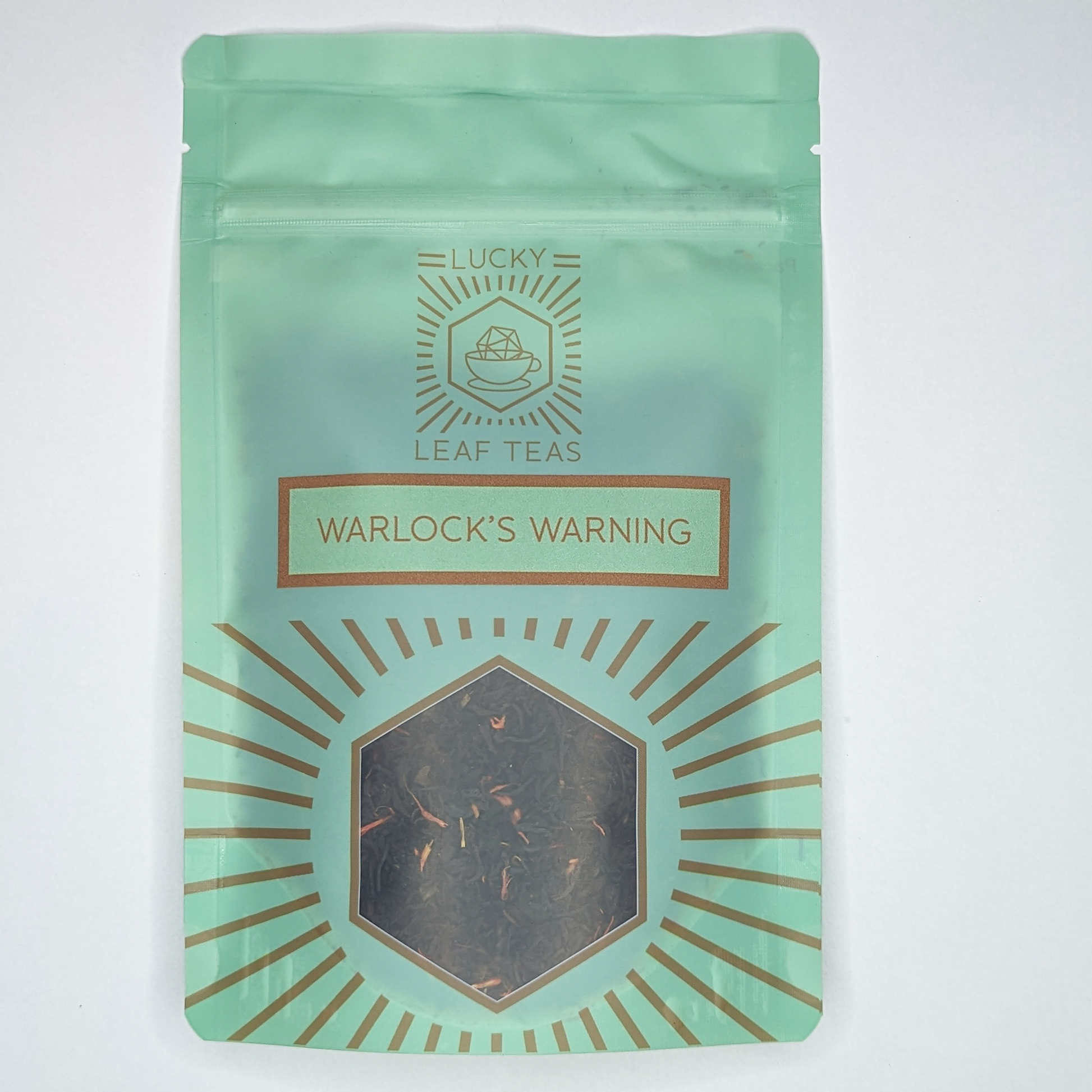 A mint-green package containing 50g of Warlock’s Warning: a black tea blend with visible red safflower petals. The name is stickered on the front, below the Lucky Leaf Teas Logo and above a hexagonal window displaying the tea.