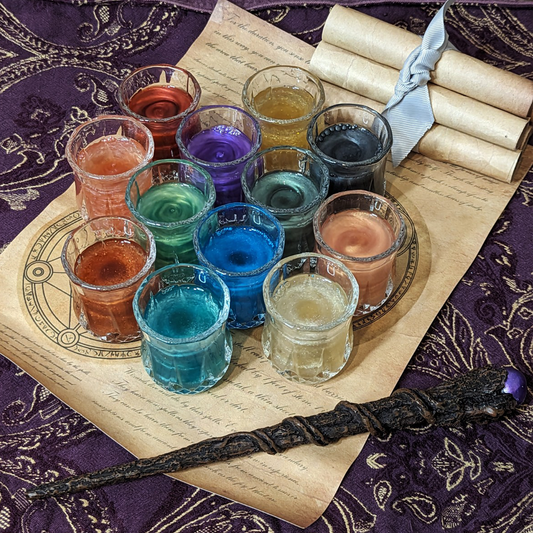 A set of twelve shot glasses on top of a spell scroll. Each one holds glittering liquid in a different colour.