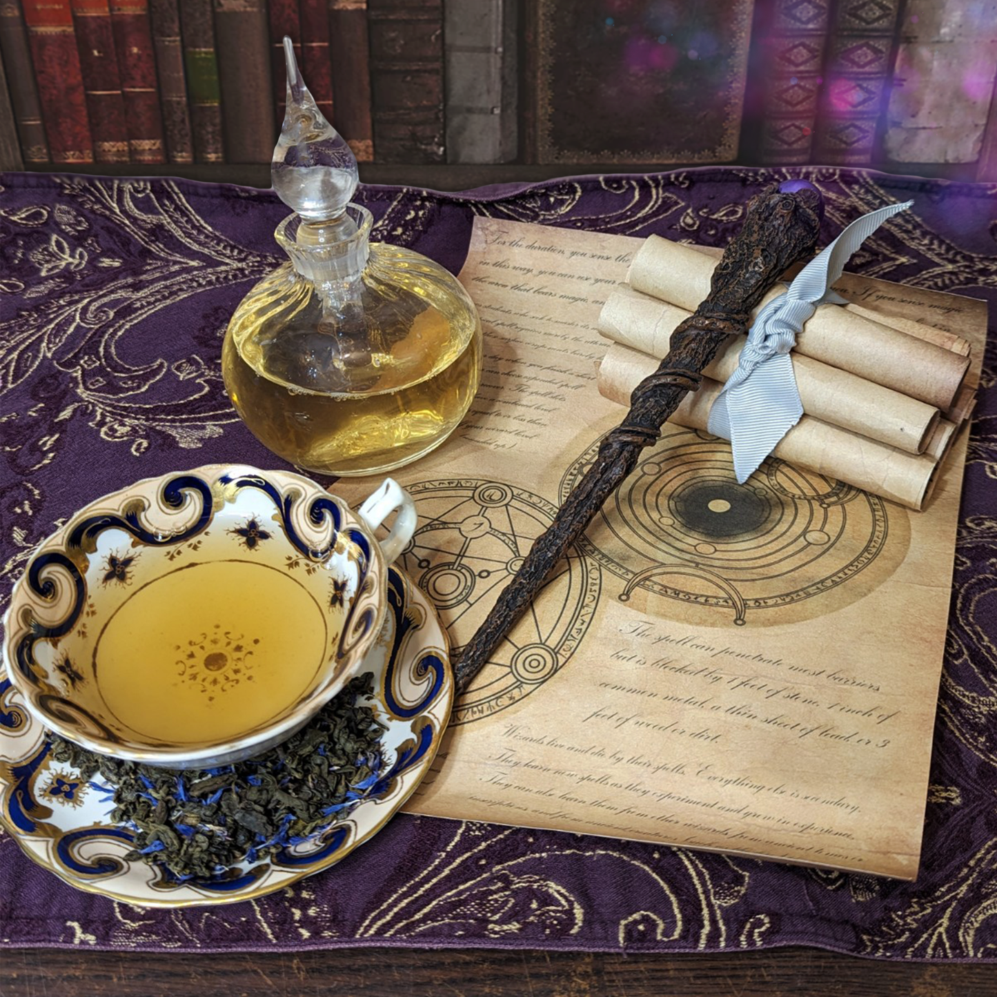 A glass potion bottle and white teacup on top of a spell scroll, next to a wand. Both are filled with pale yellow liquid.