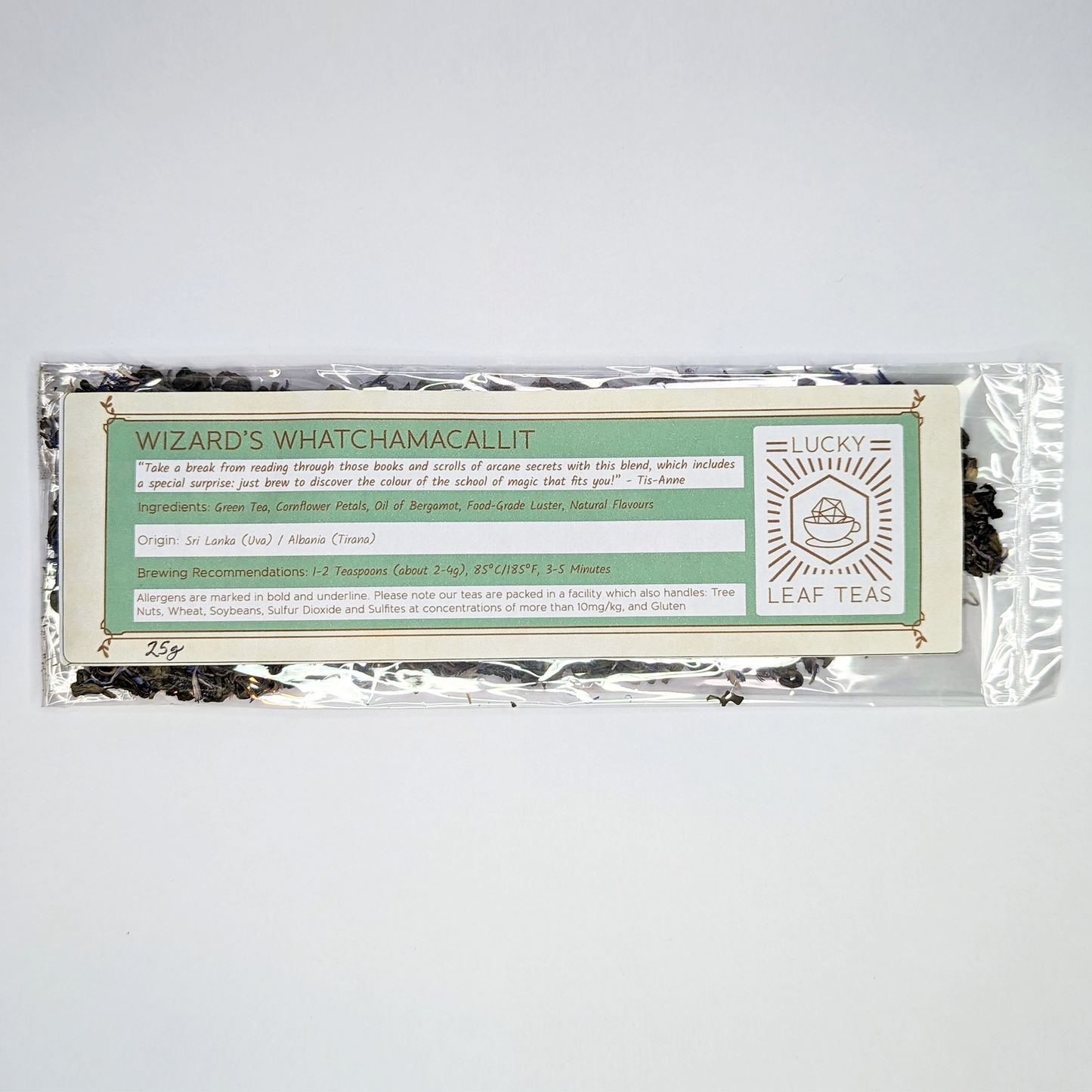 A slim, see-through package containing 25g of Wizard’s Whatchamacallit: a green tea blend with visible blue cornflower petals. A label with the name, ingredients, origin and brewing recommendations is printed on the front, next to the Lucky Leaf Teas Logo.